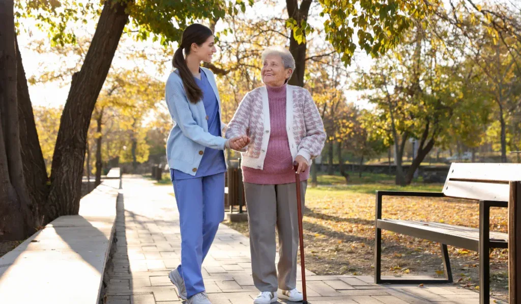 Elderly woman with walking cane and her caregiver in park